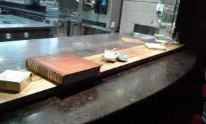 Tavolo dello Chef: Fino a un totale di cinque persone ha la possibilità di consumare il pasto ricevendolo direttamente dal cuoco sul bancone e veder lavorare la brigata attraverso il vetro.